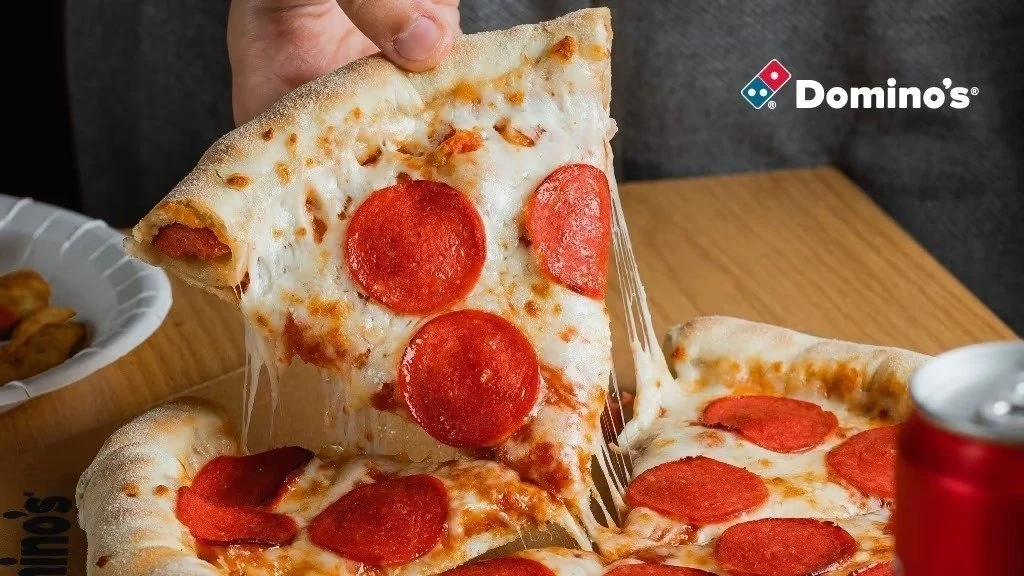Кусок пепперони с тянущимся сыром над коробкой Domino's — обложка точки в Wolt
