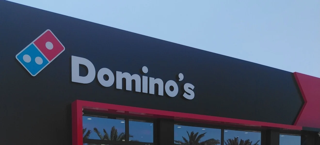 Вывеска Domino's на чёрном фасаде пиццерии в Sea Breeze — крупно